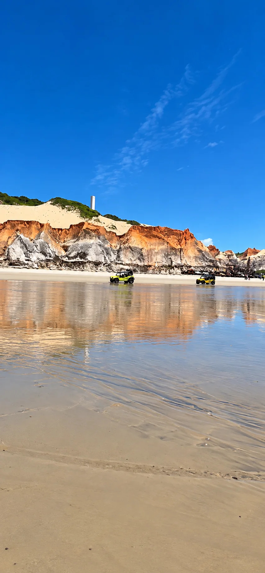 Buggys amarelos na praia, com falésias laranja refletidas na água